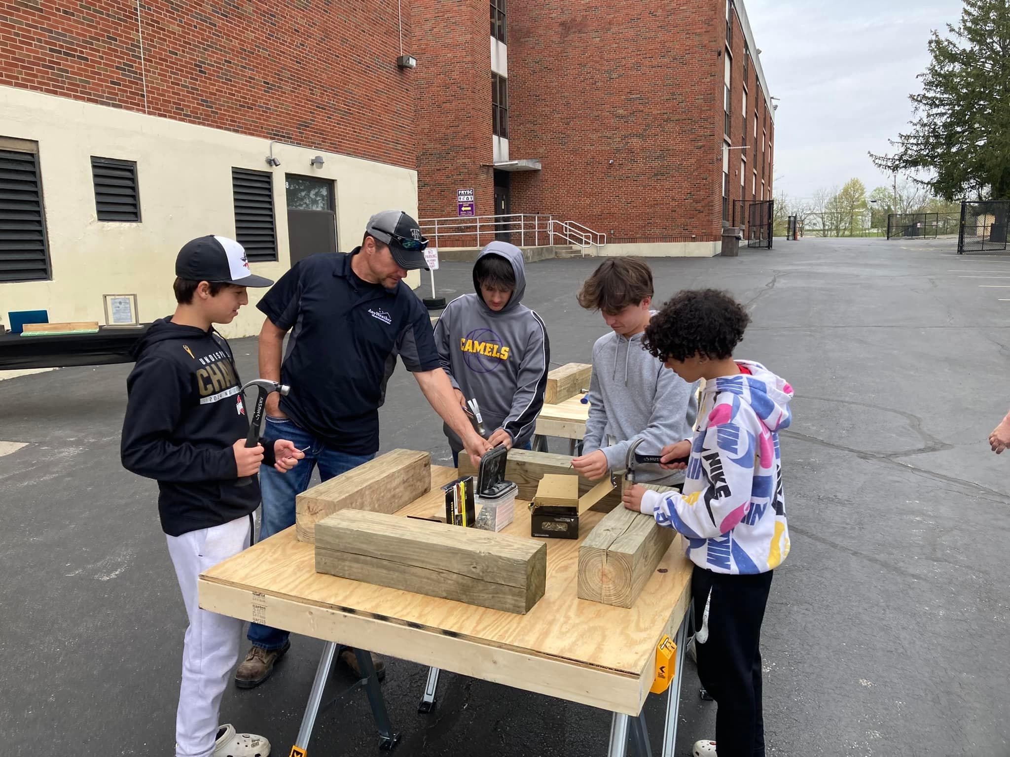 Middle school students and an instructor working with hammers and timber at an outdoor workbench during a TradesNKY BUILD lesson